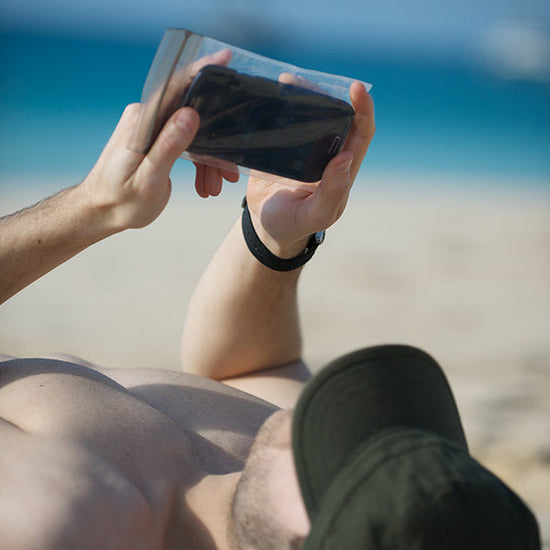 Person holding a smartphone on a beach keeping sand out with a travel bag