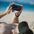 Person holding a smartphone on a beach keeping sand out with a travel bag