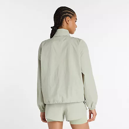 new balance athletics packable jacket for women, light wind breaker jacket that packs away into built in bag, light green colour, woman wearing nb jacket with matching shorts from behind