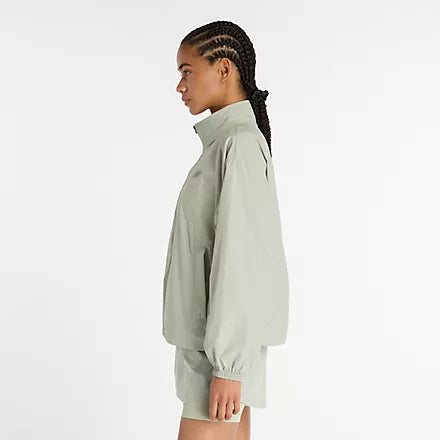 new balance athletics packable jacket for women, light wind breaker jacket that packs away into built in bag, light green colour, woman wearing nb jacket with matching shorts side profile