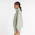 new balance athletics packable jacket for women, light wind breaker jacket that packs away into built in bag, light green colour, woman wearing nb jacket with matching shorts side profile