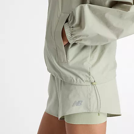 new balance athletics packable jacket for women, light wind breaker jacket that packs away into built in bag, light green colour, woman wearing nb jacket hands in pockets with matching shorts close up of pockets side profile