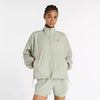 new balance athletics packable jacket for women, light wind breaker jacket that packs away into built in bag, light green colour, woman wearing nb jacket hands in pockets with matching shorts