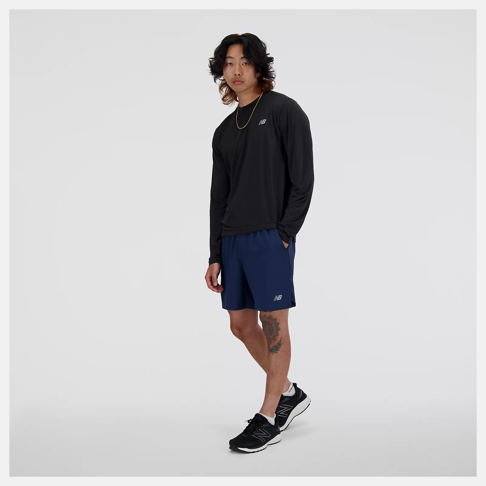 nb athletics long sleeve shirt for men, breathable long sleeve shirt good for layering, black colour, man wearing black nb long sleeve with silver nb logo and navy shorts and black new balance shoes
