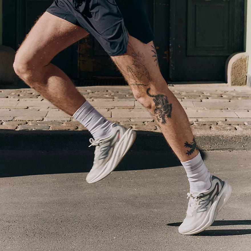 nb supercomp rebel mens, lightweight speed training and racing shoe, white and cream with black and red details, close up of mans legs running in shoes on concrete