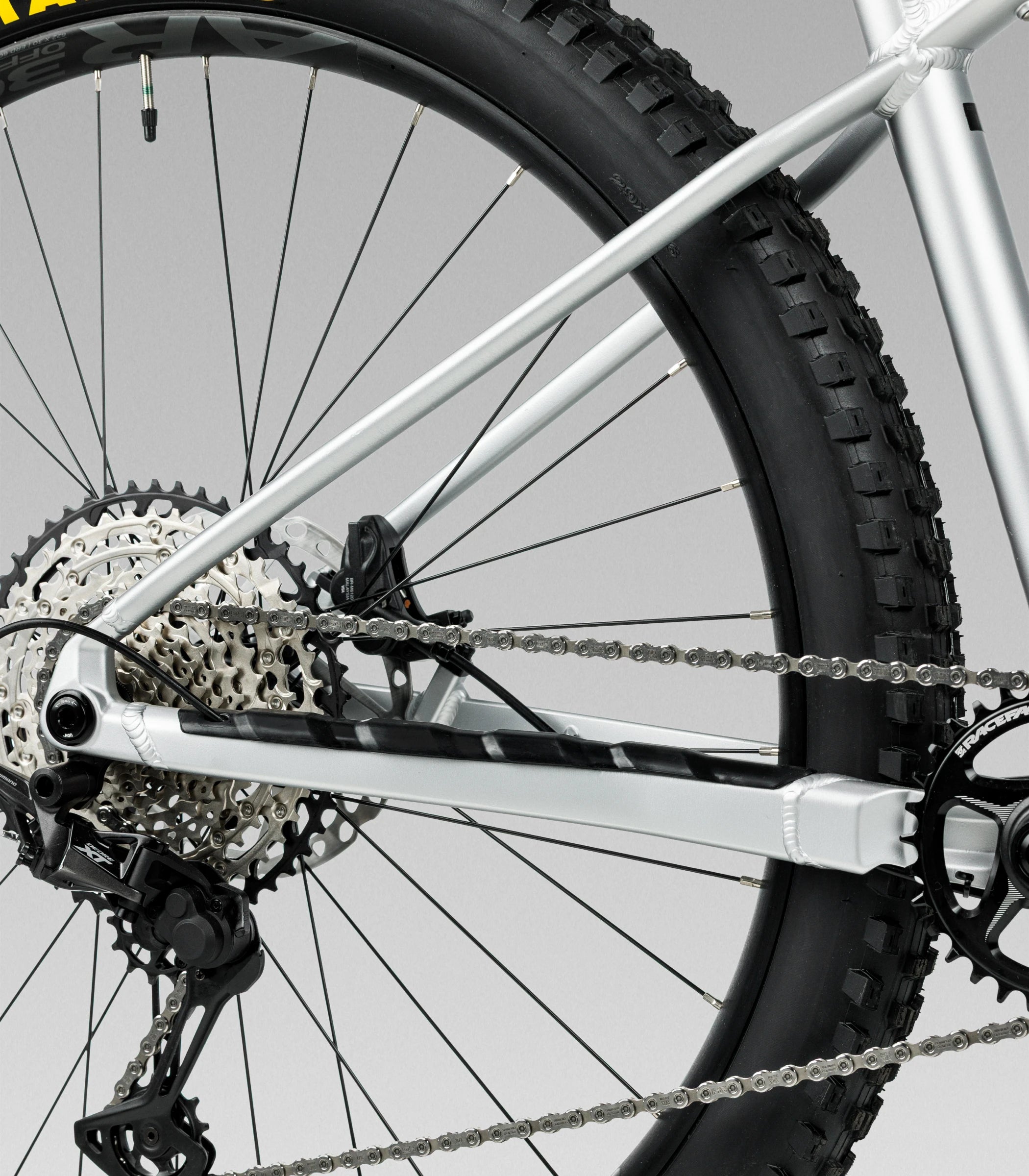 Close-up of a laufey silver mountain bike frame showing the rear wheel, chainring, cassette, derailleur, and tire 