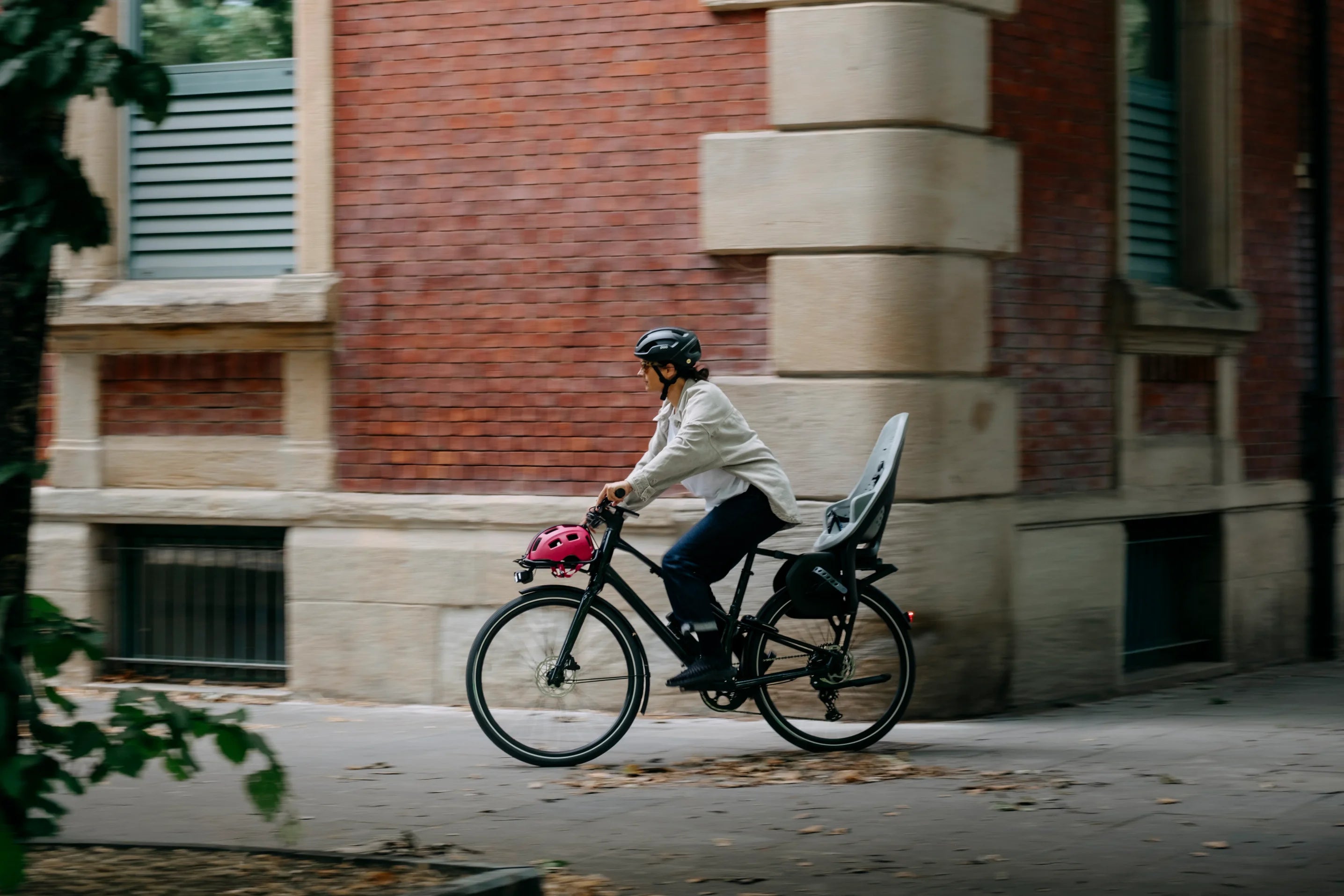 a person cycling the urban orbea vector bike through city with child seat on the back bike rack, and helmet on the front rack