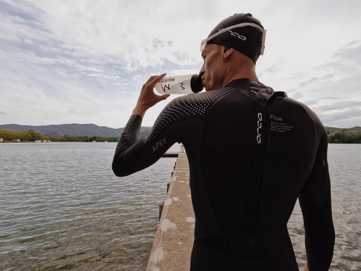 Man standing by sea in Orca apex flow triathlon wetsuit, staying hydrated with Maurten electrolytes