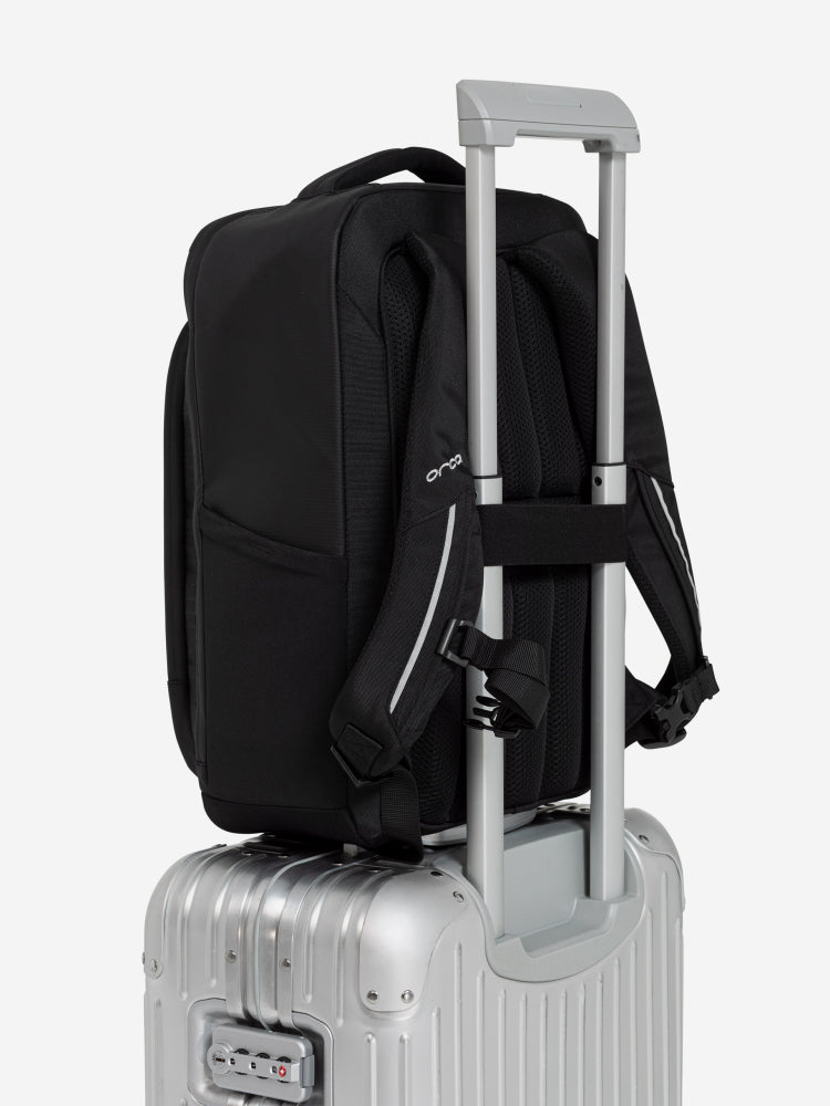 orca casual backpack in black, with soft and comfortable lower back support and space for a 15 inch laptop. Picture of backpack on a suitcase with a white background.