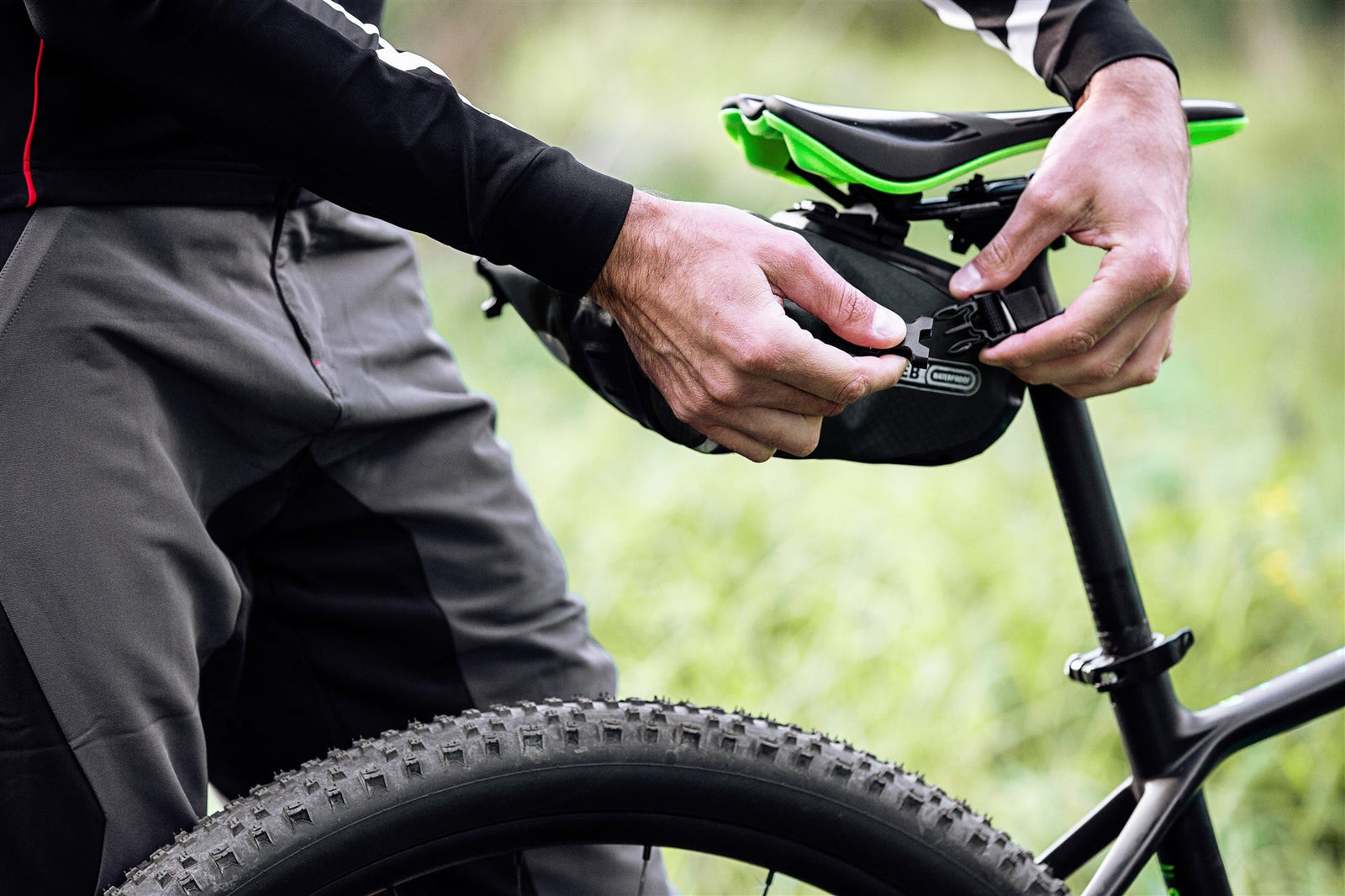 Person adjusting an ortlieb bike sadle bag on a bicycle seat with a blurred natural background