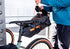 Person attaching a black ortlieb seat pack, saddle bag with orange straps to a bicycle.