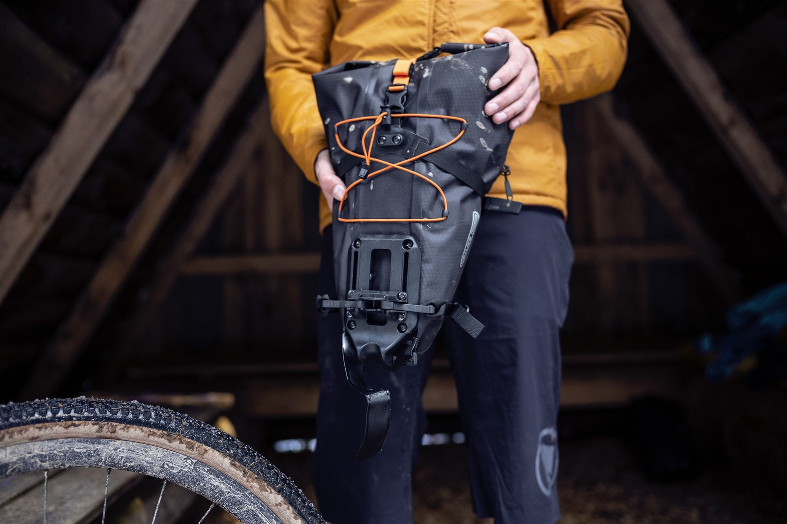 Person holding a black ortlieb bike pack, bikepacking bag with orange accents in an indoor setting.