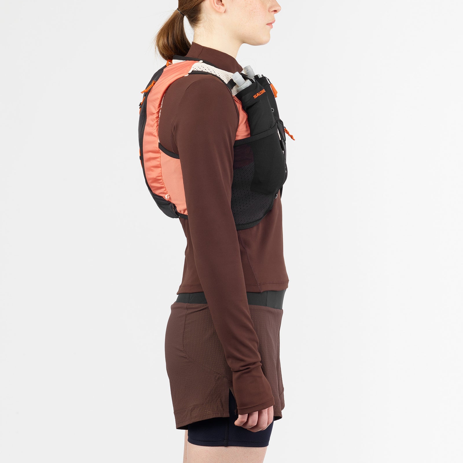 salomon active skin 4, lightweight breathable hydration running vest, woman wearing a dark grey running vest side profile with orange back