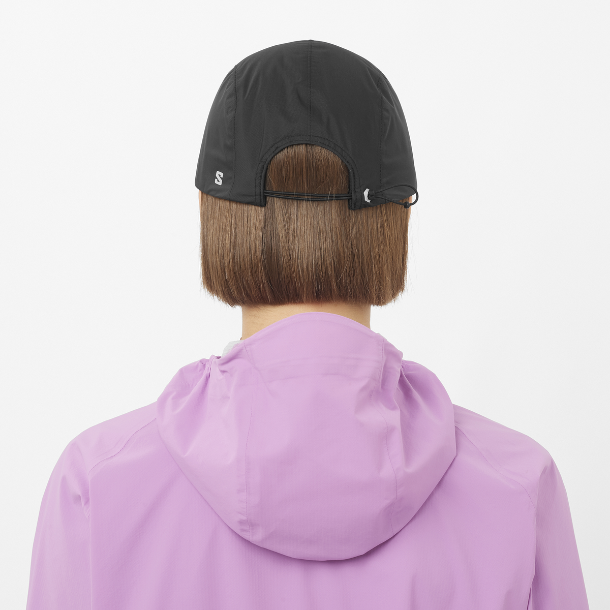 salomon bonatti pro cap with five panels, waterproof cap for running, black colour with a white logo, back view model wearing salomon cap with pink salomon jacket 