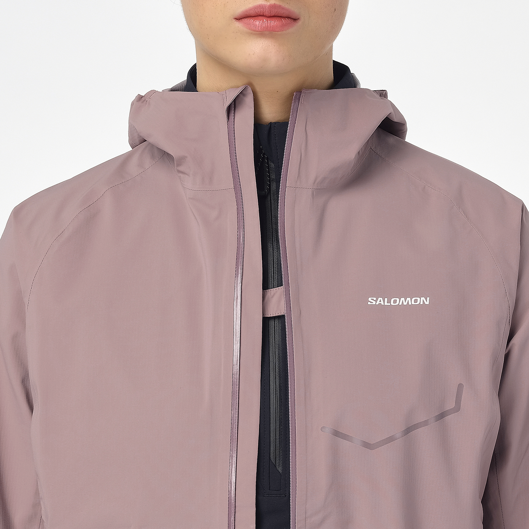 Woman wearing the salomon bonatti waterproof jacket, in antler colour, close up of button feature on chest to prevent jacket opening in the wind
