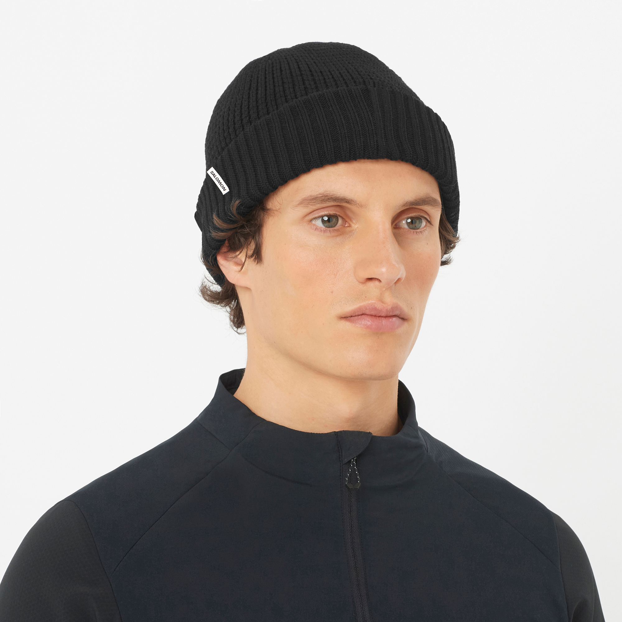 salomon docker beanie, wool blend hat for warmth and comfort, black colour, man wearing salomon beanie with black jacket on a white background
