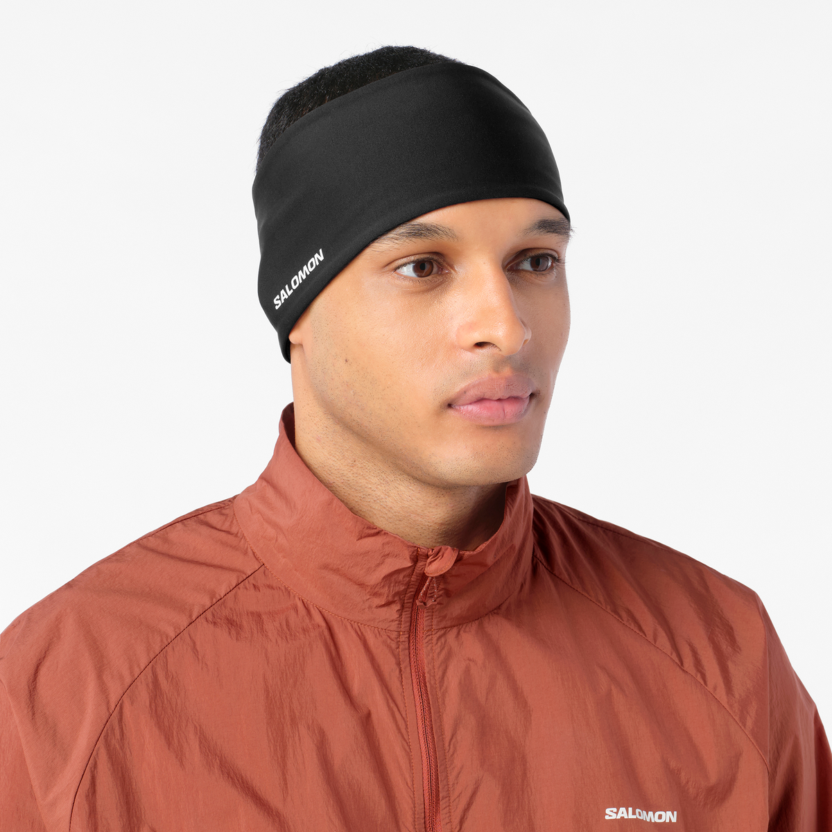 salomon run tech headband for all gender, warm and water repellent head accessory for running,  black colour with reflective salomon logo, close up of man wearing salomon headband with a burgundy top on a white background