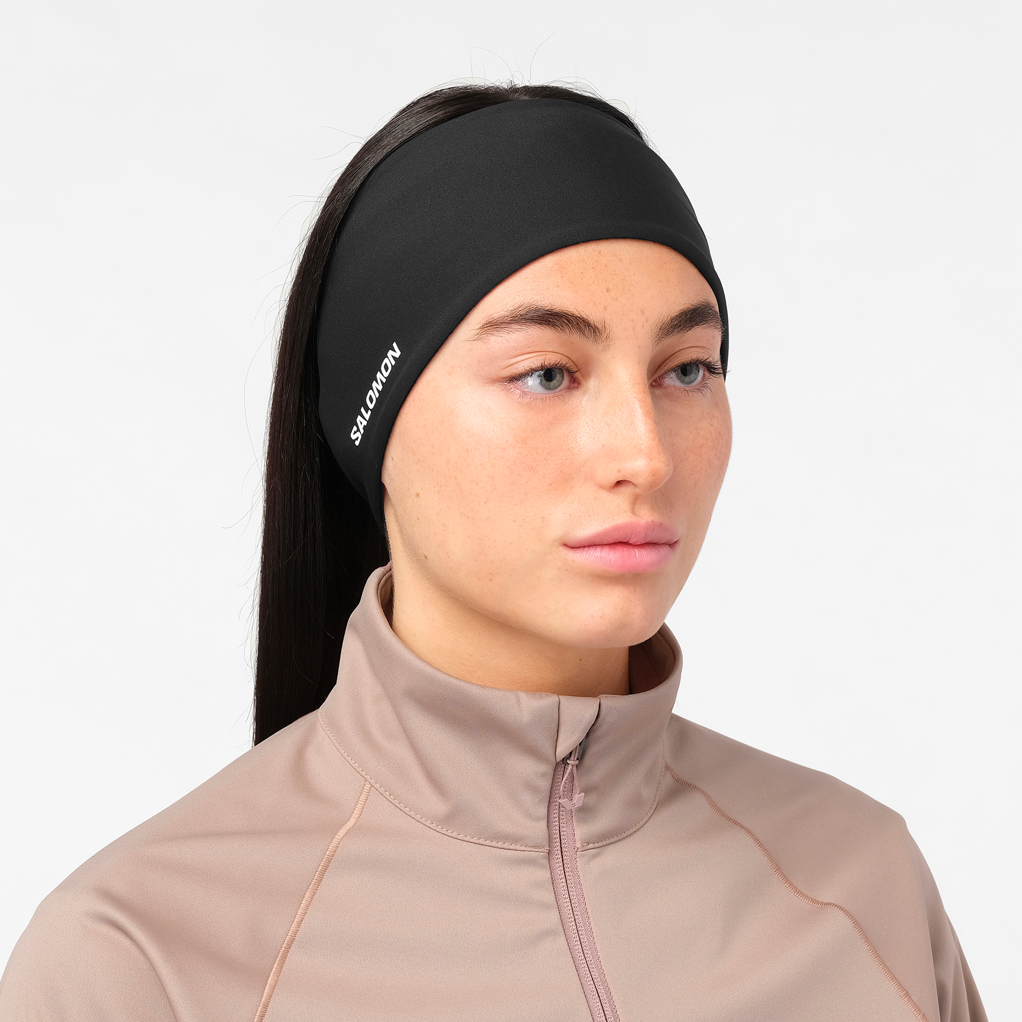 salomon run tech headband for all gender, warm and water repellent head accessory for running, black colour with reflective salomon logo, close up of woman wearing salomon headband with a grey top on a white background