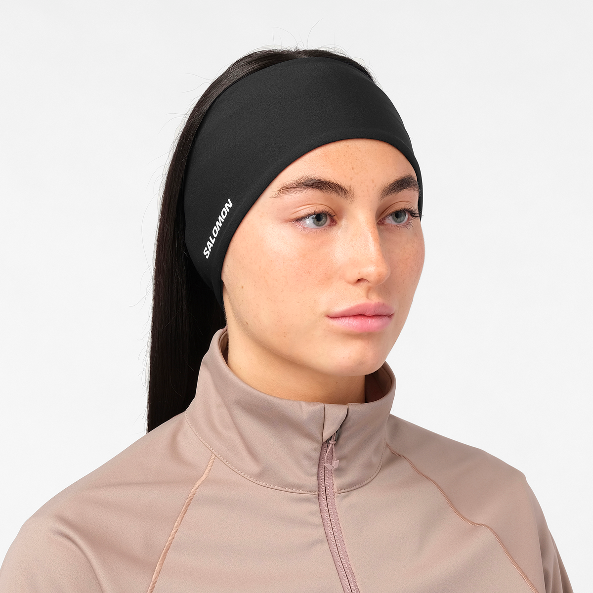 salomon run tech headband for all gender, warm and water repellent head accessory for running, black colour with reflective salomon logo, close up of woman wearing salomon headband with a grey top on a white background