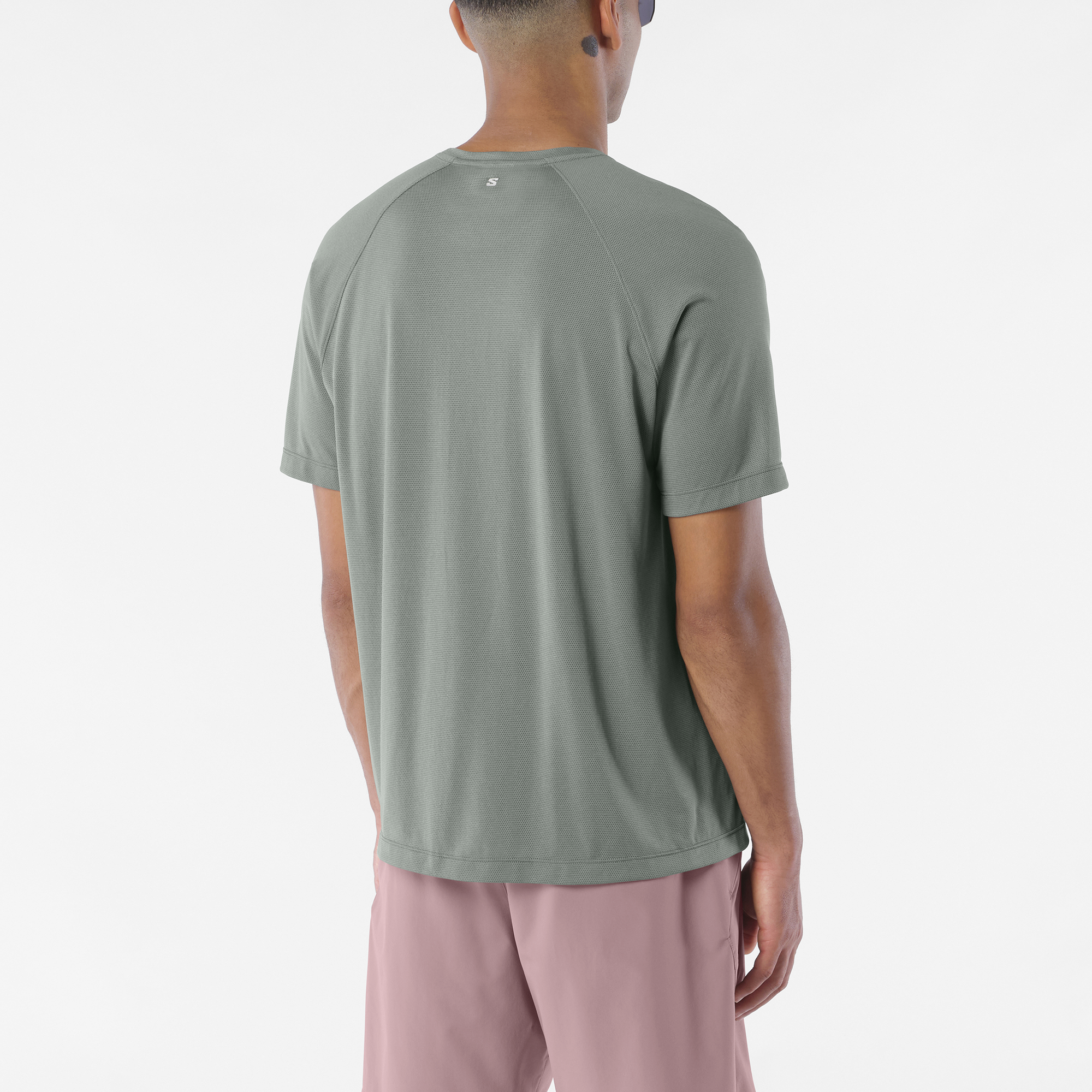 salomon shakeout core short sleeve t-shirt for men, lightweight run tee, grey colour with reflective salomon logo, back view of man wearing salomon tee on a white background with pink shorts