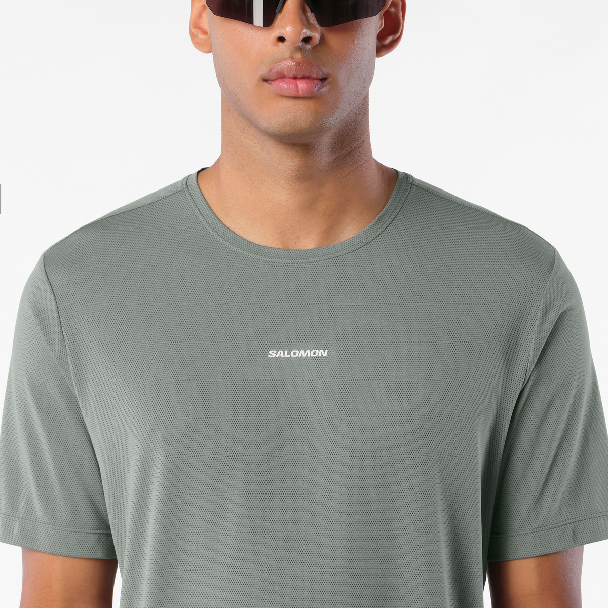 salomon shakeout core short sleeve t-shirt for men, lightweight run tee, grey colour with reflective salomon logo, close up of man wearing salomon tee on a white background 