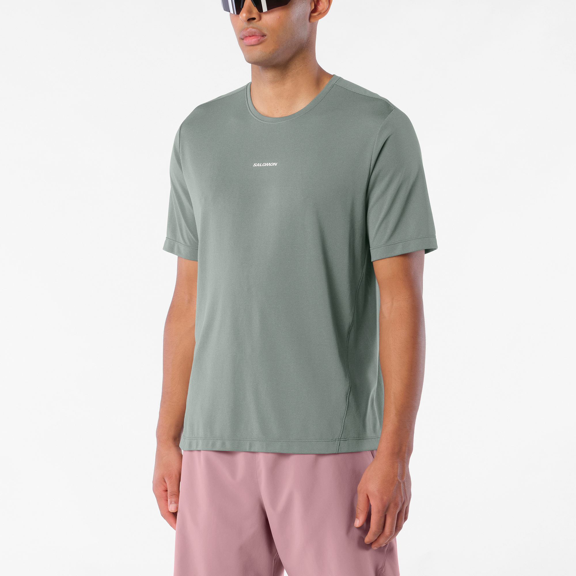 salomon shakeout core short sleeve t-shirt for men, lightweight run tee, grey colour with reflective salomon logo, man wearing salomon tee on a white background with pink shorts