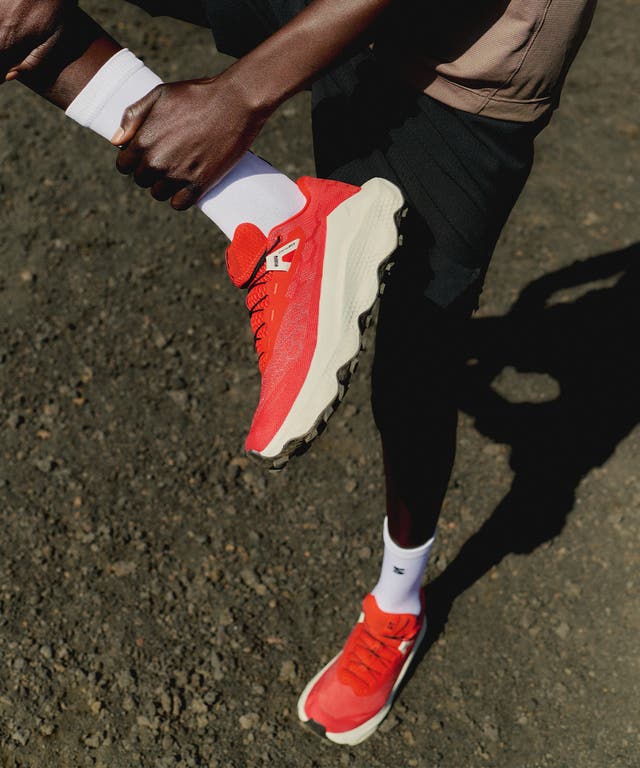 mens salomon ultra glide 4, mens trail shoe in the fiery red, vanilla ice, black colourway. picture of model wearing the shoes on a trail.