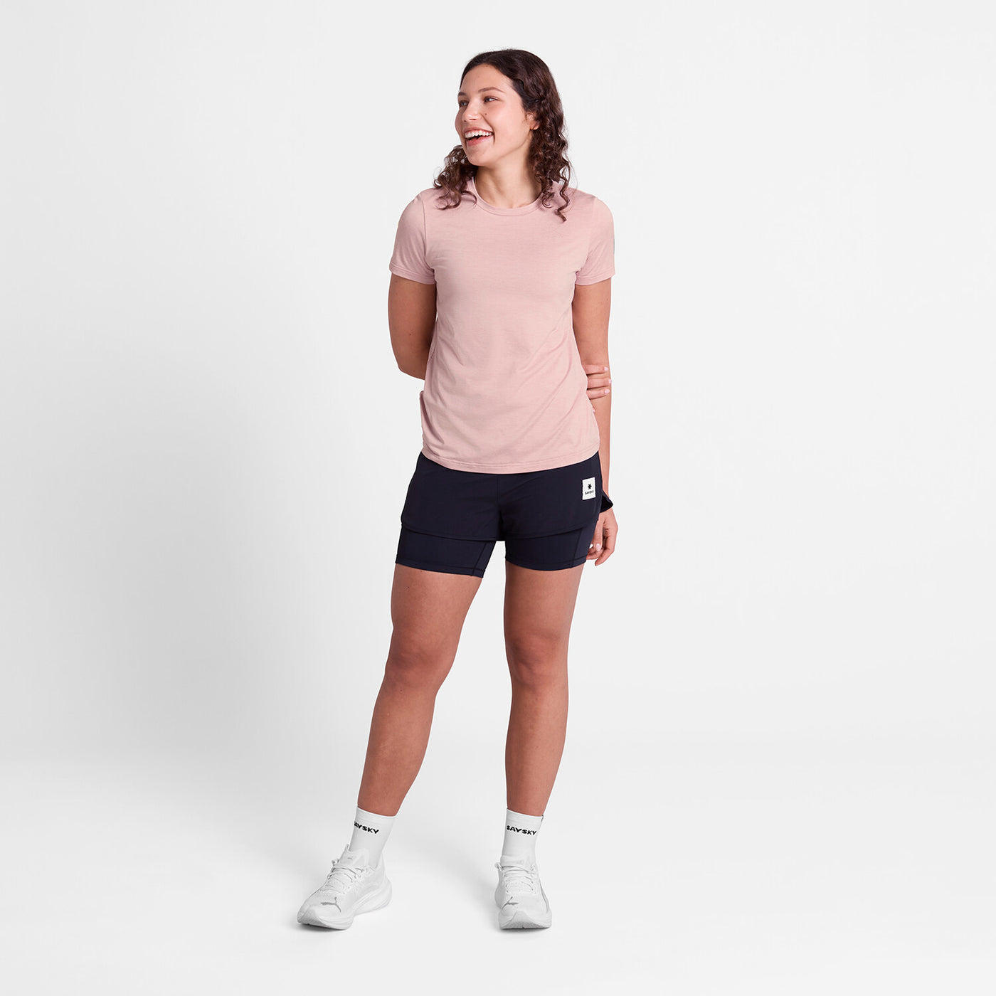 Women's light pink short-sleeved running t-shirt by SAYSKY, full-body shot of a woman wearing pink t-shirt and black shorts