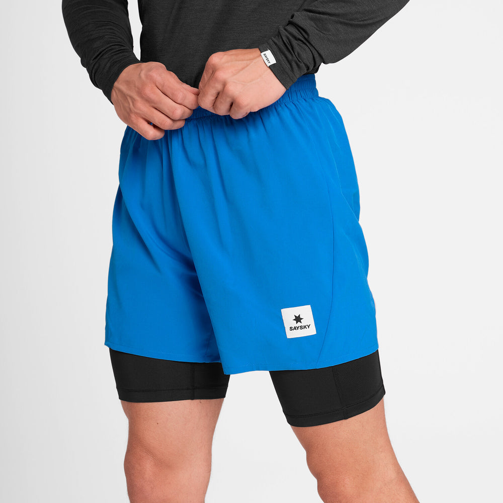 close up of man wearing bright blue saysky 2 in 1 run short with black inner and logo on front with black long sleeve top