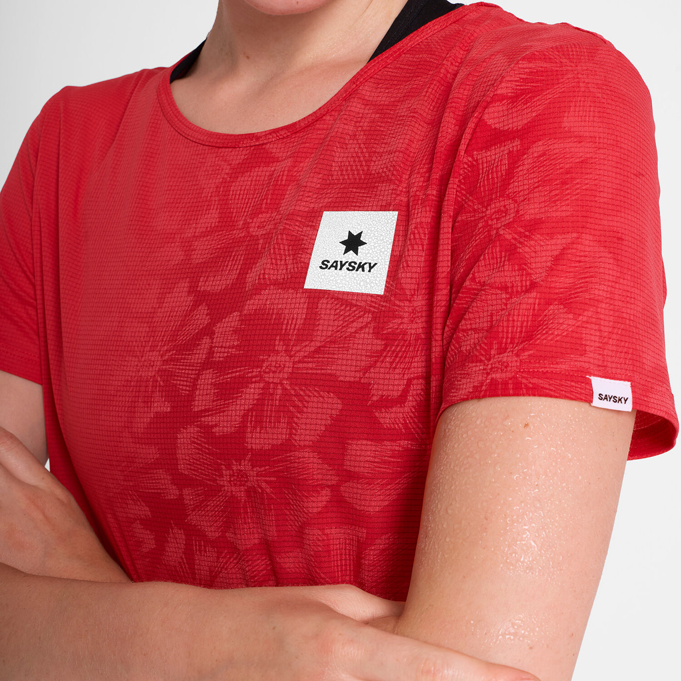 woman wearing saysky run tee in red colour, with logo at front, flower pattern shows when tee is wet