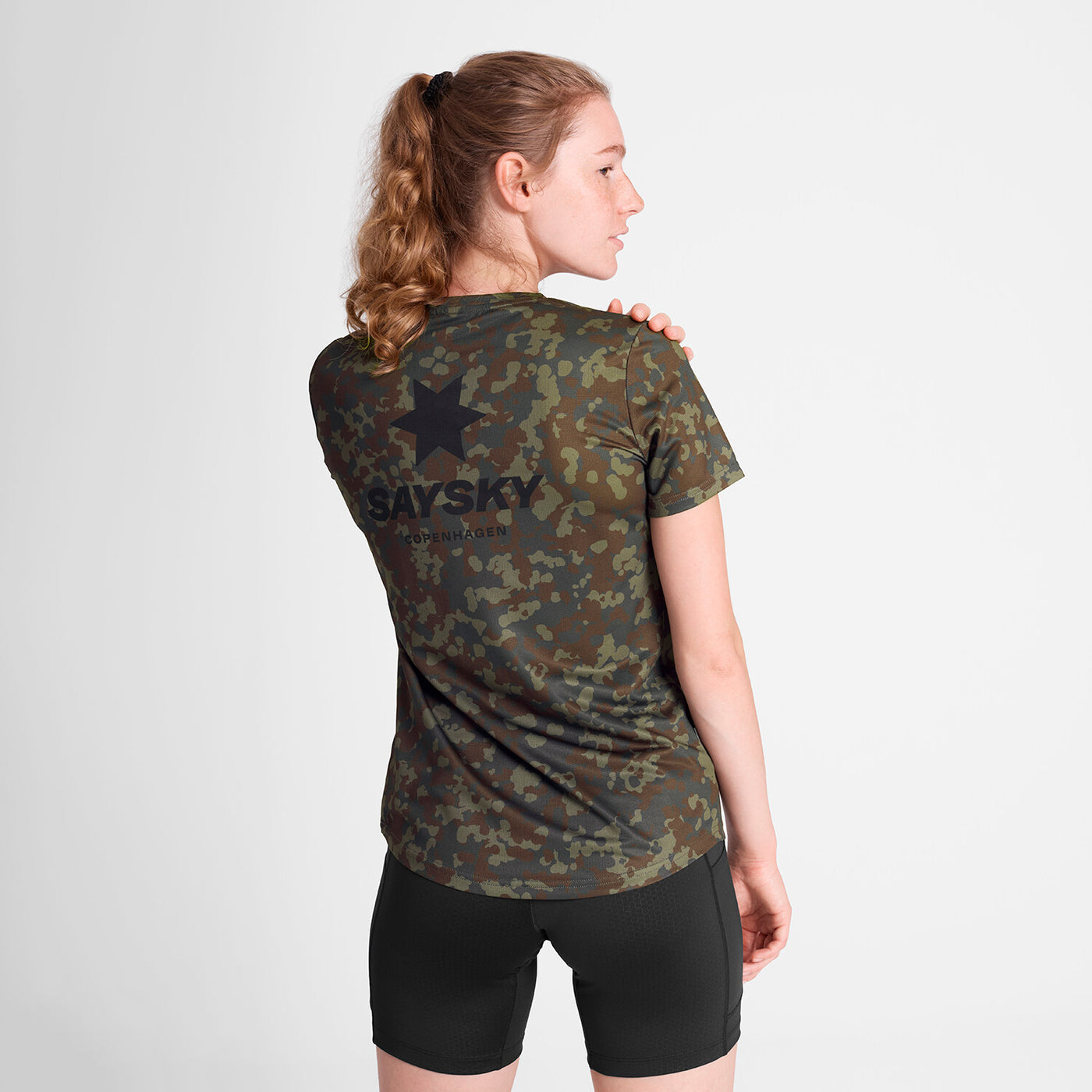 saysky lightweight running t-shirt for women, breathable and quick dry material,  brown and green camouflage colour, back profile of woman wearing saysky t-shirt with black shorts on a white background