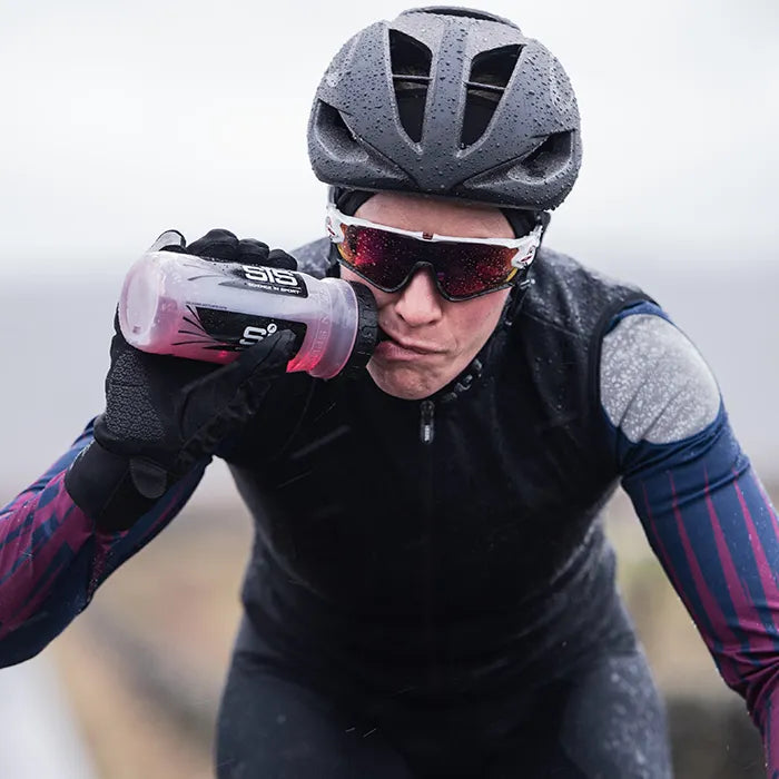 Cyclist in winter gear drinking SiS hydration tablets from a water bottle 