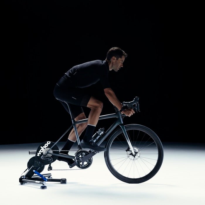 wahoo kickr smart trainer, indoor cycling trainer, black colour, person cycling with trainer attached to back of bike