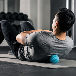 Man lying on his back using a massage ball to relieve tension in his upper back area